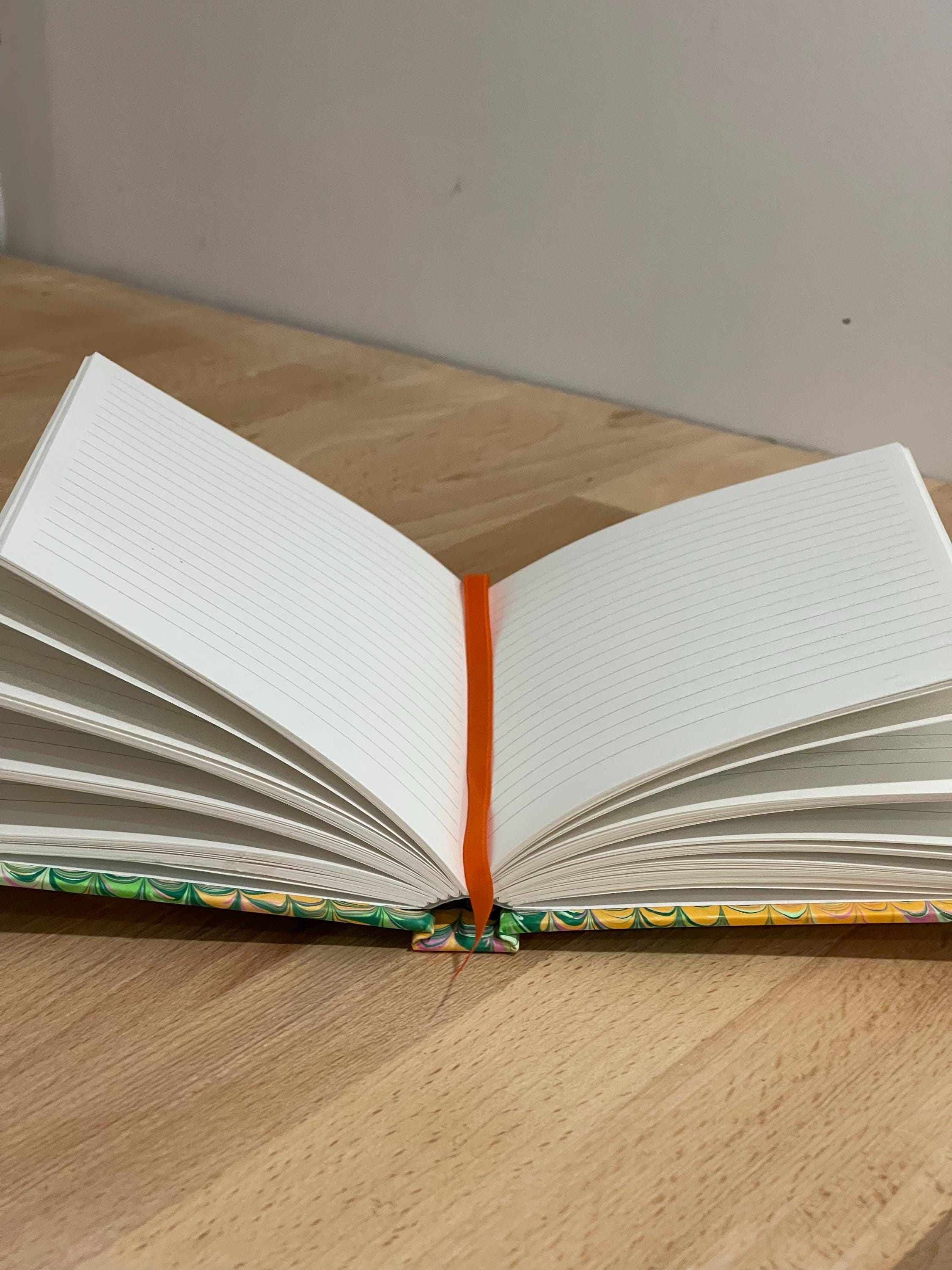 Hand marbled/painted notebook journal in a green and orange non pareil pattern with an orange book mark and recycled white lined pages